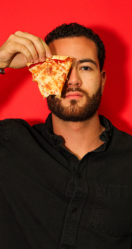 Man holding a slice of pizza up to his face against a red background