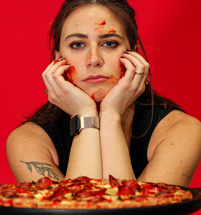 Woman with pizza on her face and hands in front of a red background